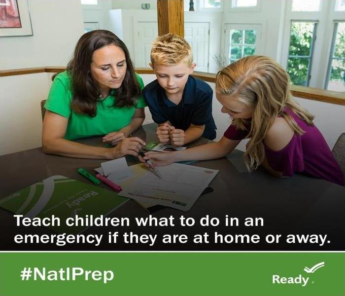 A mother with young son and daughter discussing what to do in an emergency at the kitchen table.