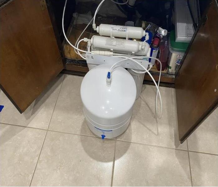 white water filtration system pulled out from underneath a sink with brown cabinets.