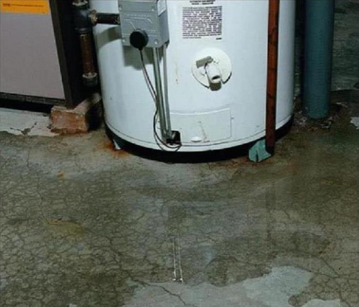 white water heater, with a water puddle on concrete floor. 