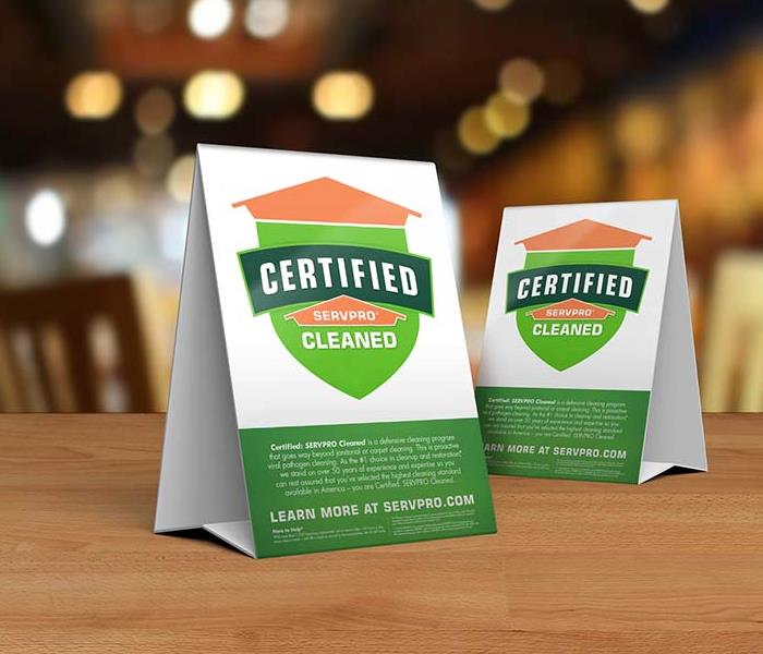 Table tent signs describing the Certified: SERVPRO Cleaned program on top of a wooden table.