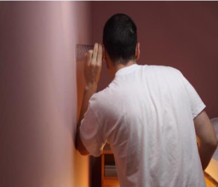 man in white t-shirt with clear glass to his ear and a wall