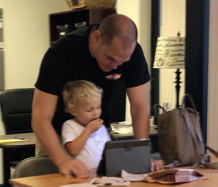 father in black t-shirt overlooking his blond son in a white t-shirt, on a tablet
