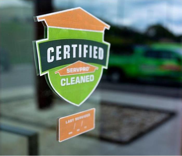 Sticker on a window with the words Certified: SERVPRO Cleaned with a reflection of a green servpro vehicle. 