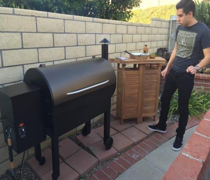 A black Smoker Grill closed against a cream brick wall and a young man standing back from grill